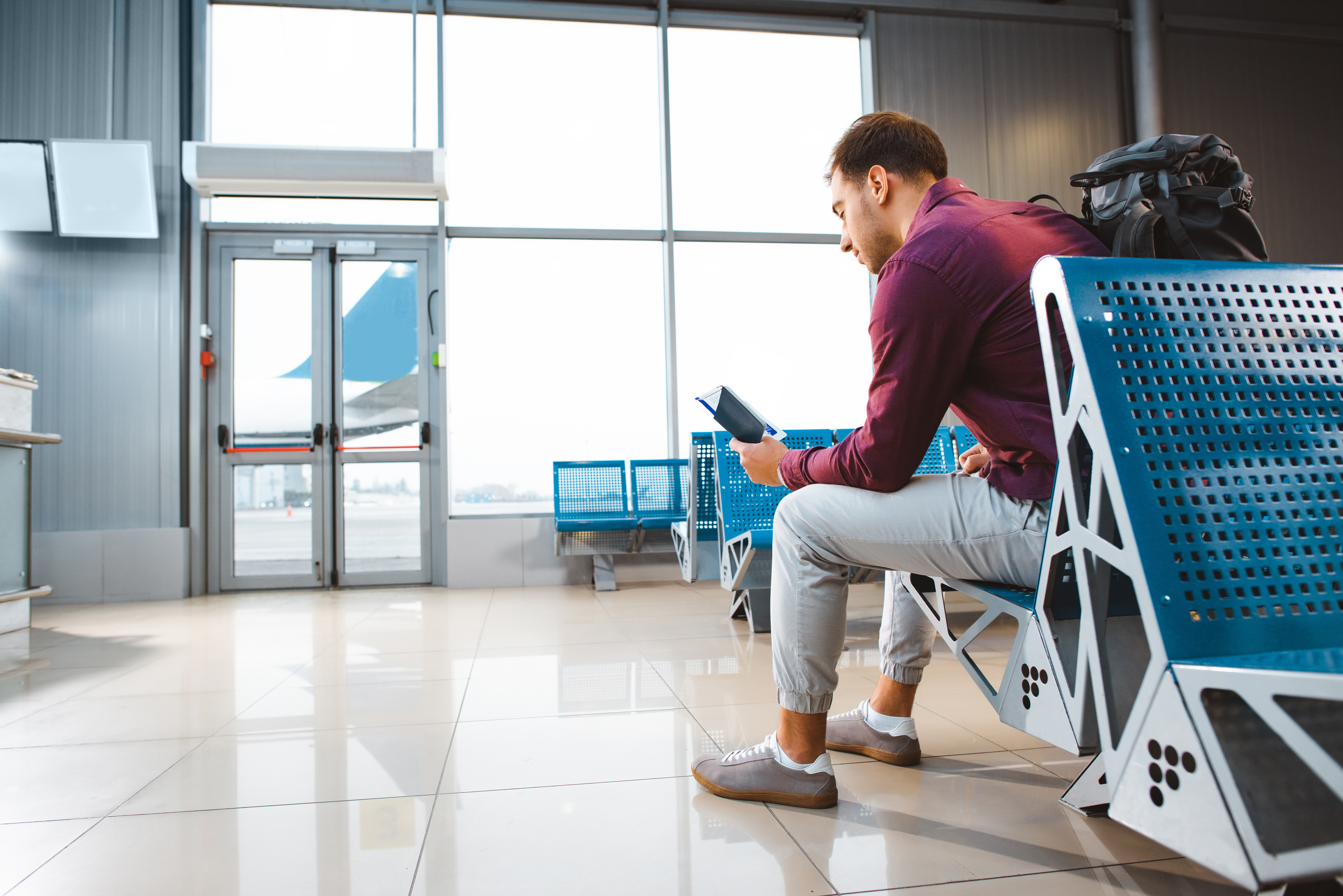 man holding passport with air ticket and sitting near gate in airport in departure lounge