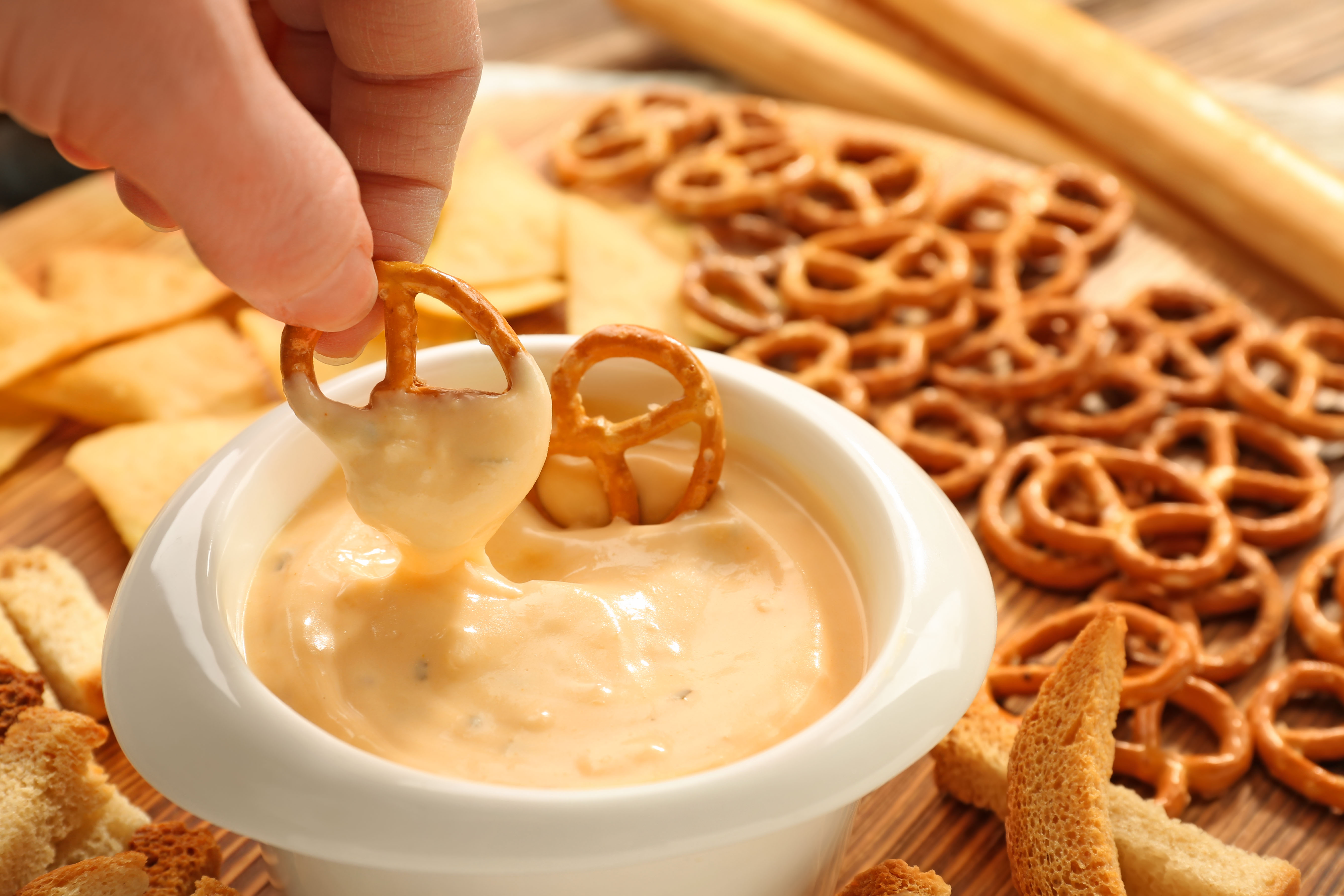 Female hand dipping pretzel in bowl with beer cheese dip, closeup